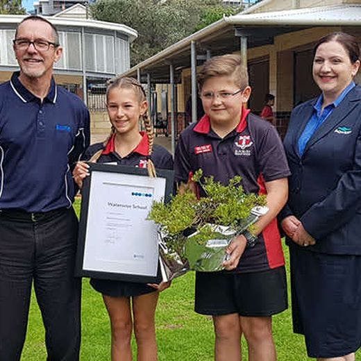 Twos students holding a plaque and a plant, standing next to two Aqwest representatives at Bunbury primary school.