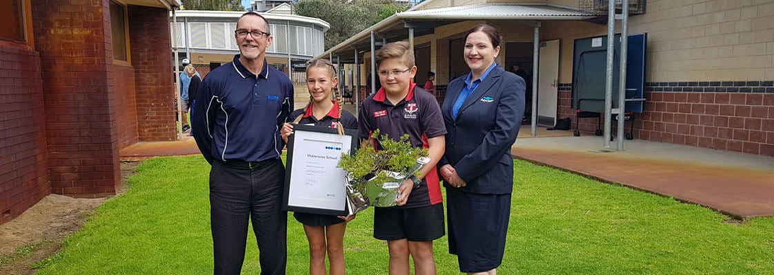 Twos students holding a plaque and a plant, standing next to two Aqwest representatives at Bunbury primary school.