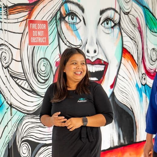 Two people walking together, talking and smiling in front of a mural.