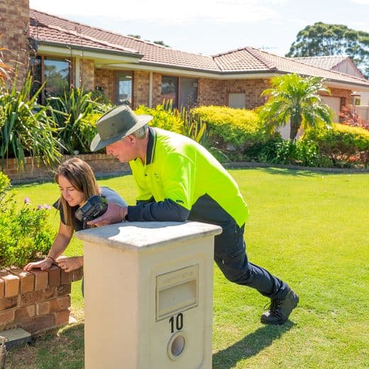 Aqwest employee with home owner looking at water connection and meter on green lawn in front of house.