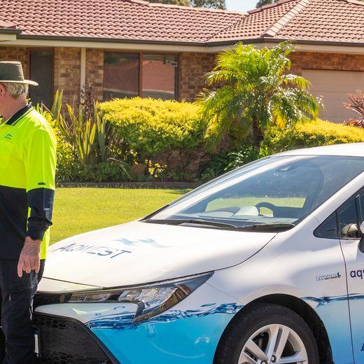 Person speaking to an Aqwest employee next to an Aqwest branded car in front of a home with green lawn.