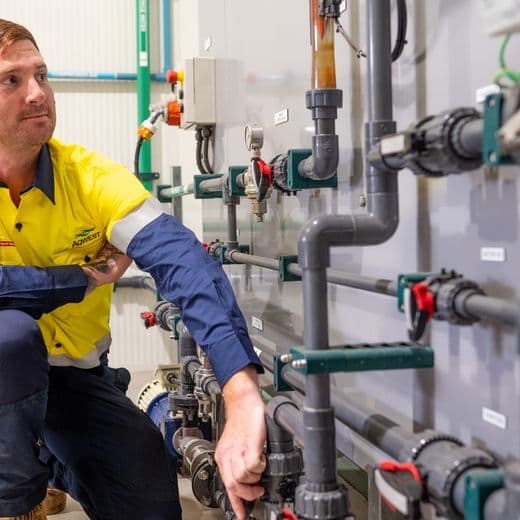 man kneeling on one knee next to a wall covered in pipes and valves.