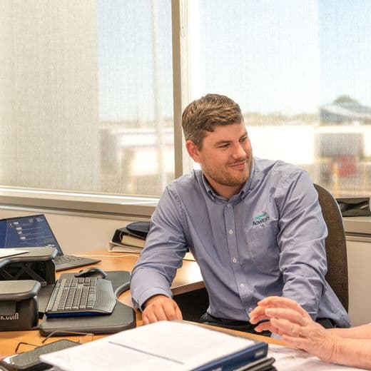 Two employee speaking at a desk.