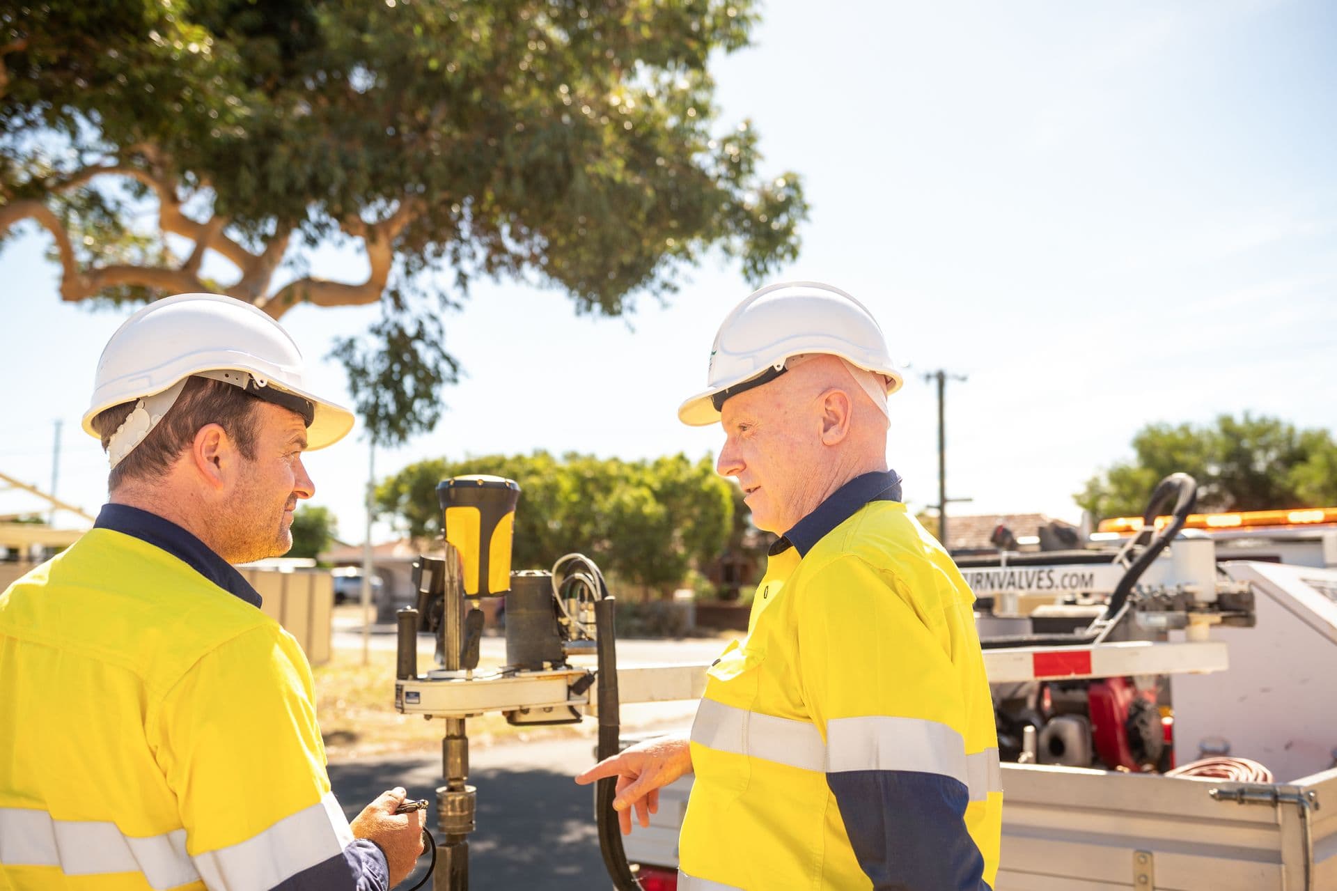 Two employees in high vis and hard hats discussing in front of monitoring equipment.