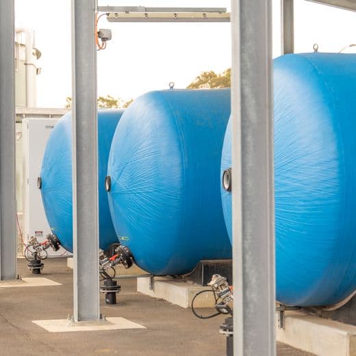 Man walking past large water containers, whilst checking his laptop.