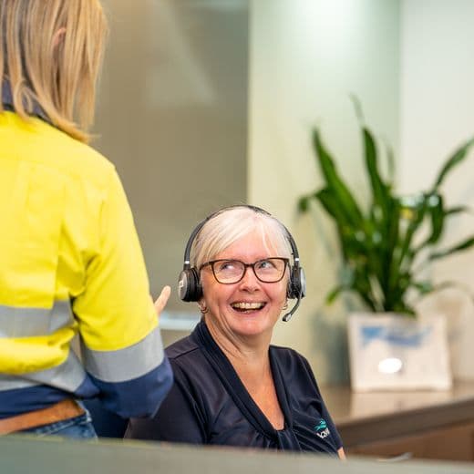 Front desk person talking to person in high-vis vest.