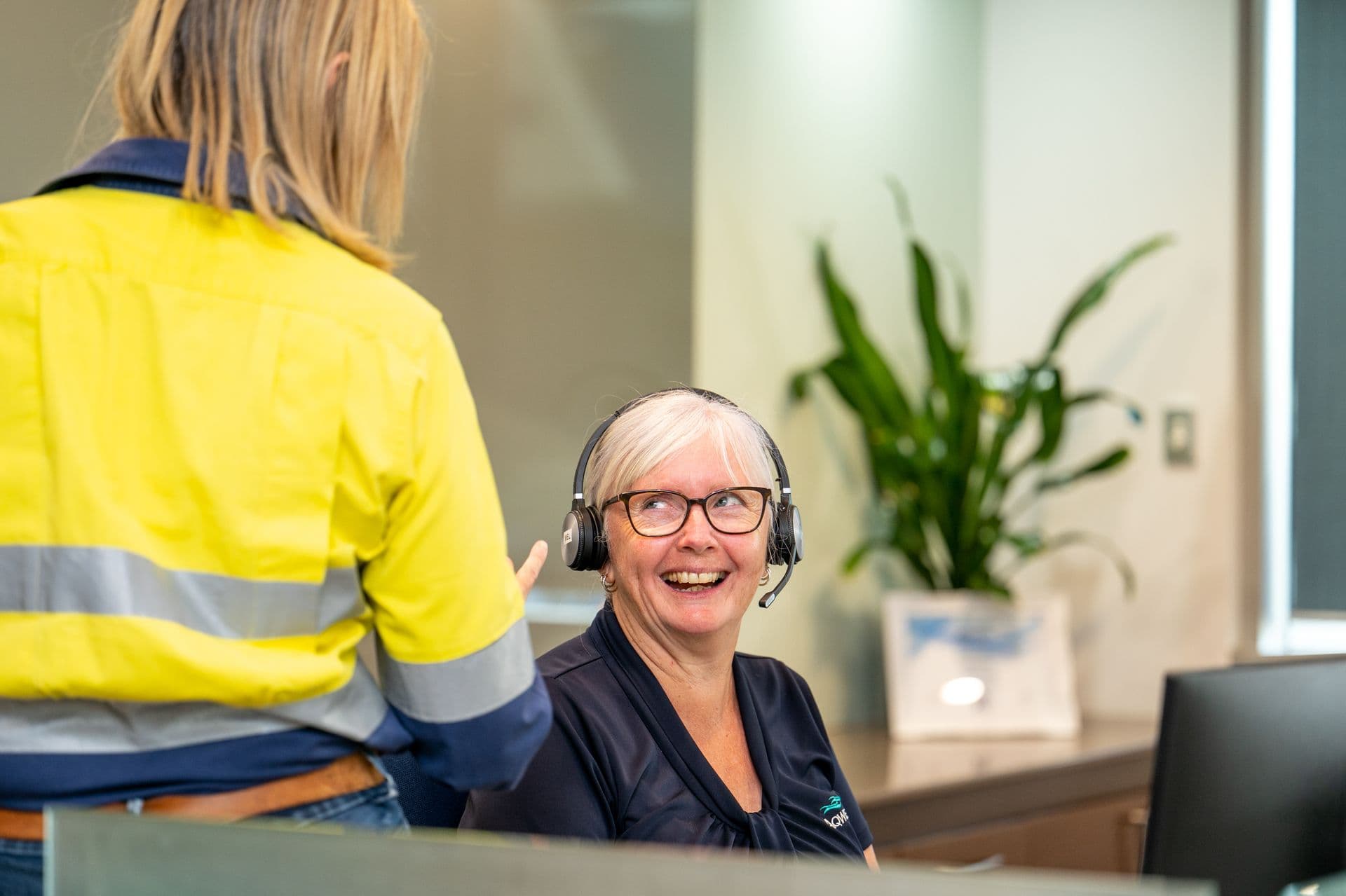 Front desk person talking to person in high-vis vest.