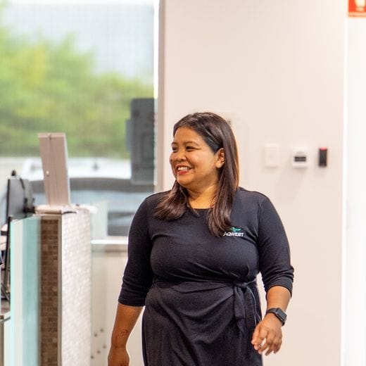 Two people walking side by side in an office, talking and smiling, reception in the background.